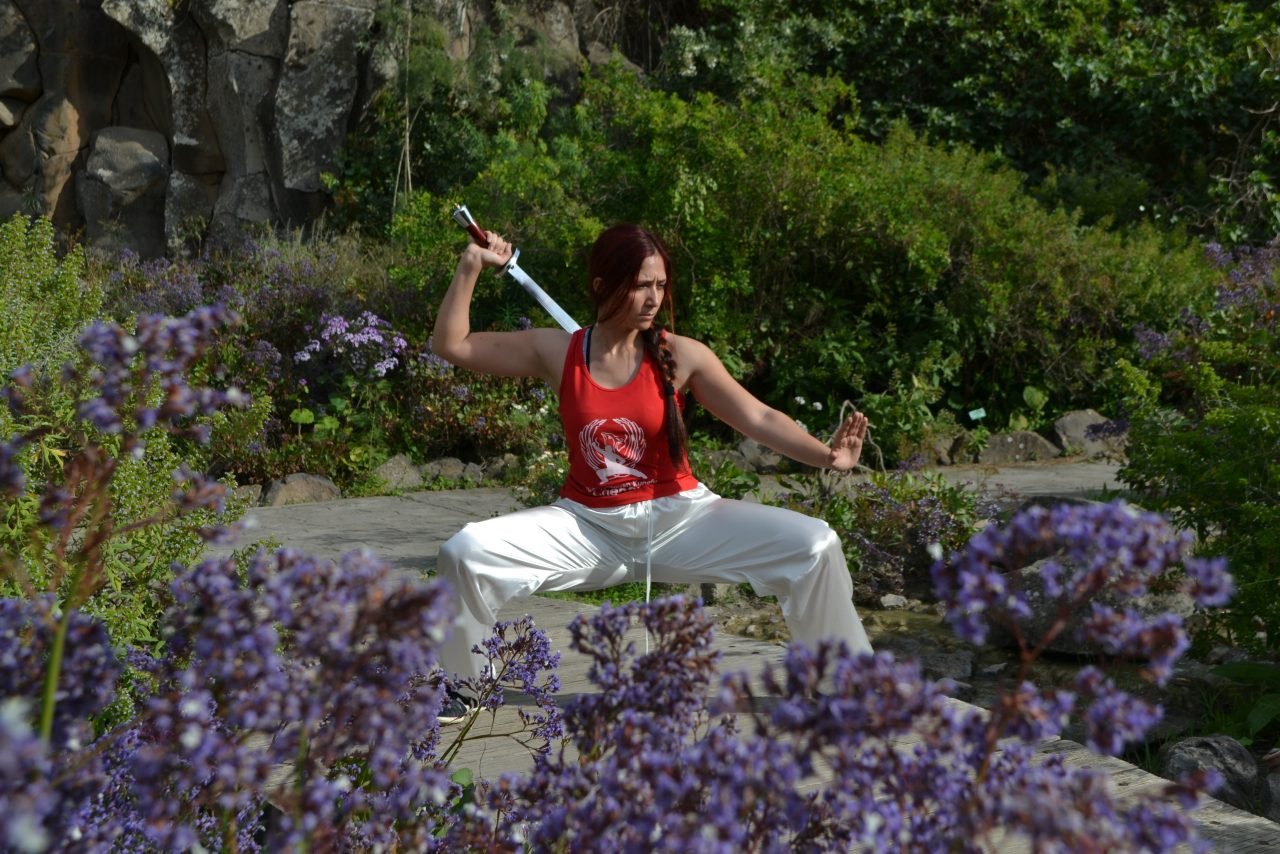 IMAGEN PROFESORA CON ESPADA PRACTICANDO ARTES MARCIALES EN JARDIN CON ESTANQUE